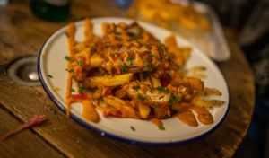 Close view of a plate of fries topped with chives, pickled onions and sauce..