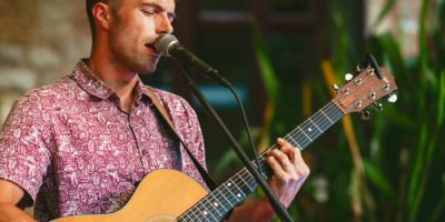 Male acoustic guitarist performing live music at The Pavilion, a popular evening activity at Mendip Basecamp family campsite, adding to the relaxed, festival-style holiday atmosphere