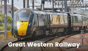 A green and yellow train engine pulls a few passenger cars. There is text on the front under the driver’s window that says ‘GWR’.